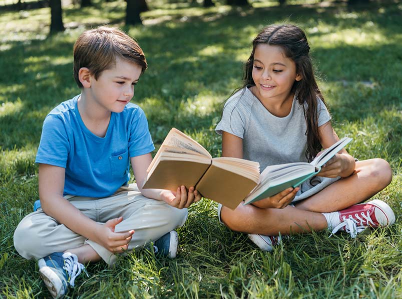 boy and girl reading homeschool books outside during summer break